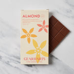 A bar of almond chocolate in its cream-colored Gearharts packaging, shown next to the dark brown chocolate bar itself on a white marble surface.