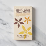 A rectangular box of Gearharts Brown Sugar Pecan Toffee chocolate, featuring a cream-colored background with brown and yellow floral graphics, set on a white marble surface.