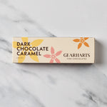 A rectangular box of Gearharts Fine Chocolates Dark Chocolate Caramel, featuring a cream-colored background with yellow, pink, and orange floral illustrations, set on a white marble surface.