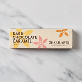 A rectangular box of Gearharts Fine Chocolates Dark Chocolate Caramel, featuring a cream-colored background with yellow, pink, and orange floral illustrations, set on a white marble surface.