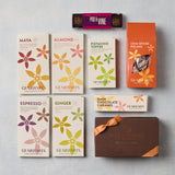 A flat lay of GEARHARTS fine chocolates and chocolate bars on a light gray textured background. The assortment includes boxes of Maya, Almond, Pistachio Toffee, Chai Spiced Pecans, Espresso, Ginger, Dark Chocolate Caramel, and a single Pod & Vine chocolate bar.